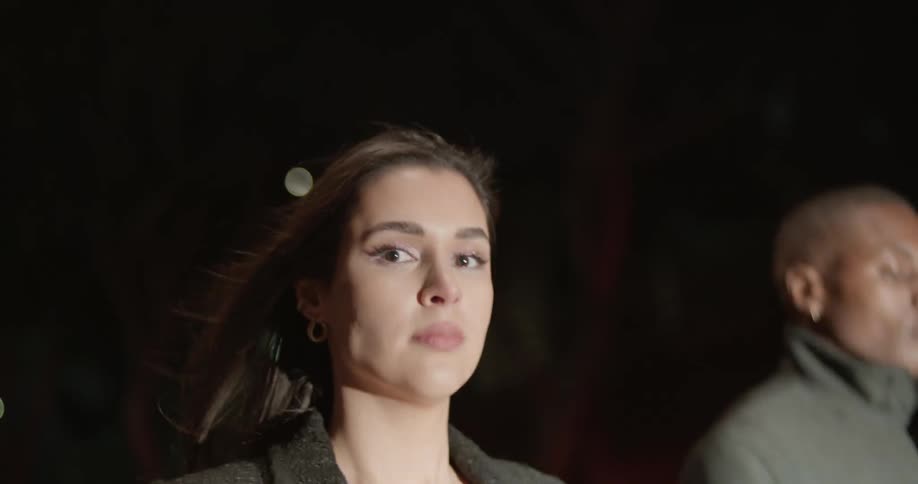 Woman stares to the side as she and others walk together at night