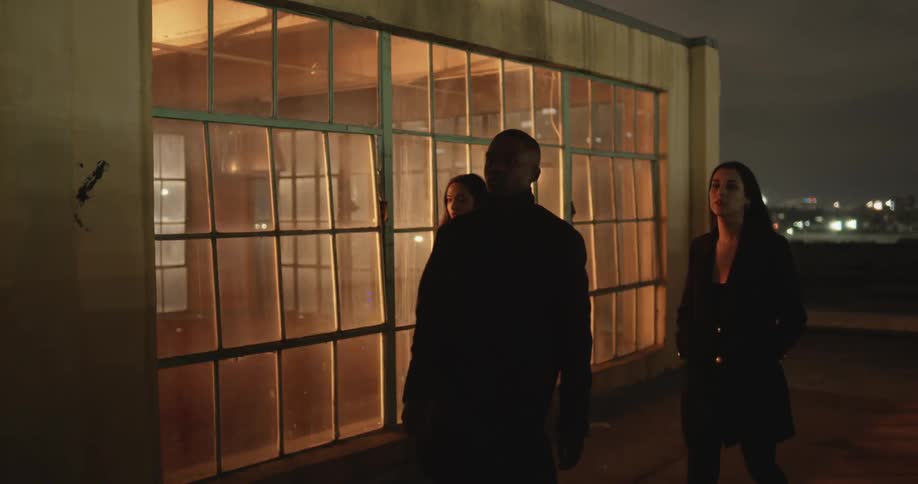 A man and two women walking on the rooftop of a tall building at night