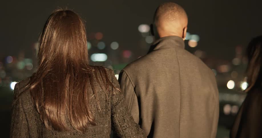 Three people on a rooftop looking out at the los angeles city skyline at night