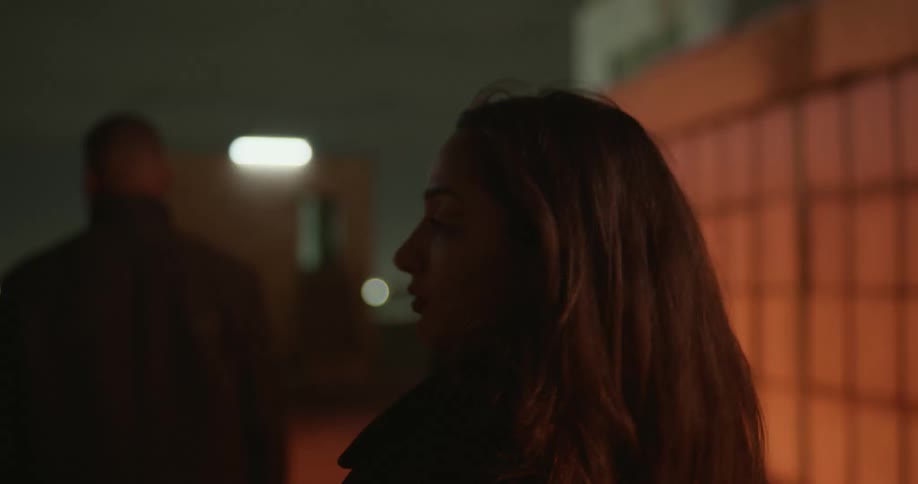 Three people walk onto roof of urban building under flashing lights at night