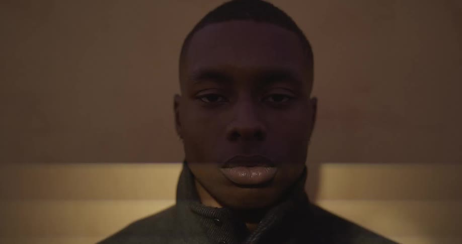 Man with short hair and black overcoat stares at camera