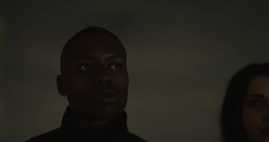 Man and woman stand motionless outdoors at night as flashing light illuminates them