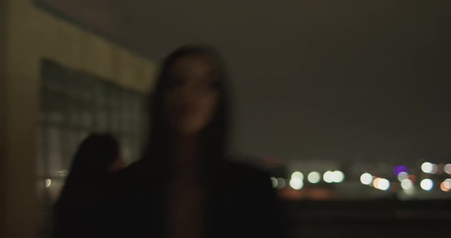Two women dressed in black are walking past a building in fast motion and turn around to look at the camera as lights flash in their faces