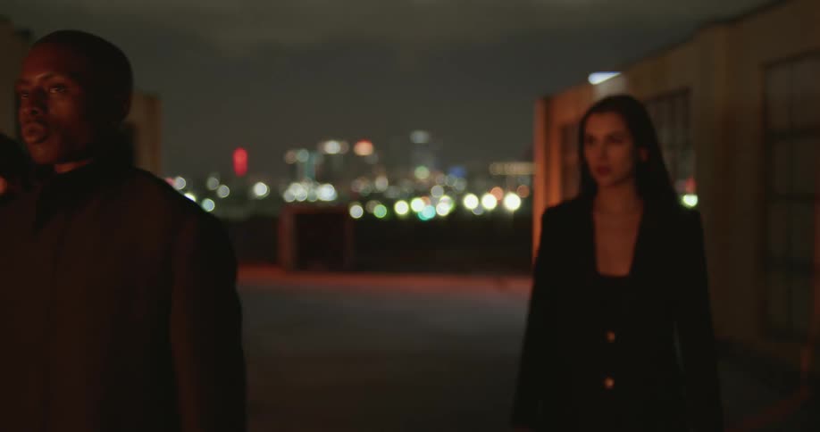 Three people walk through an alley as bright lights flash behind them