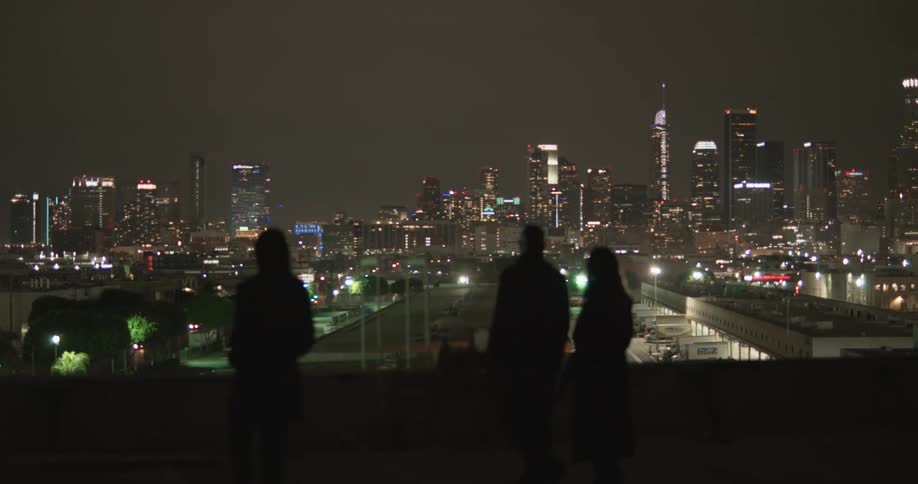 Three people walk along an overpass with views of downtown