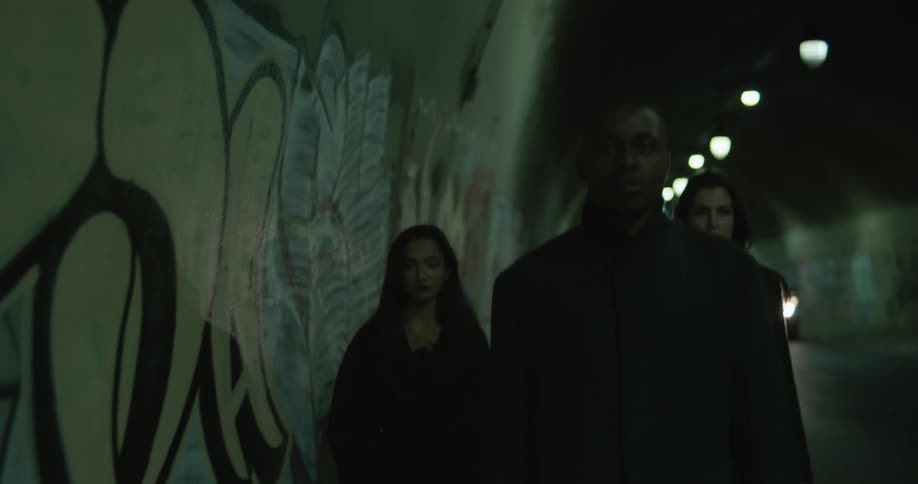 Three people walk through graffiti decorated tunnel paralleling car
