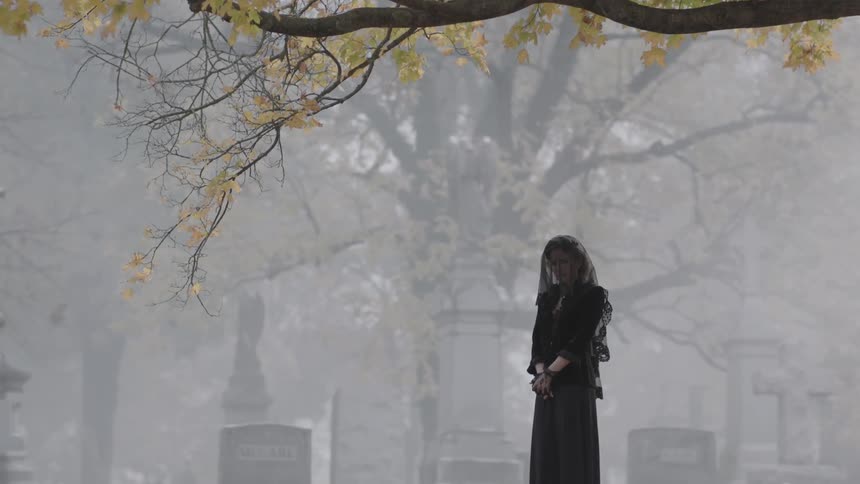 A woman in black stands mourning in a cemetery