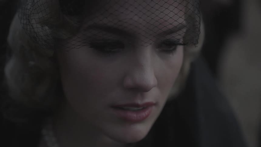 A blond woman wearing a black veil looks around