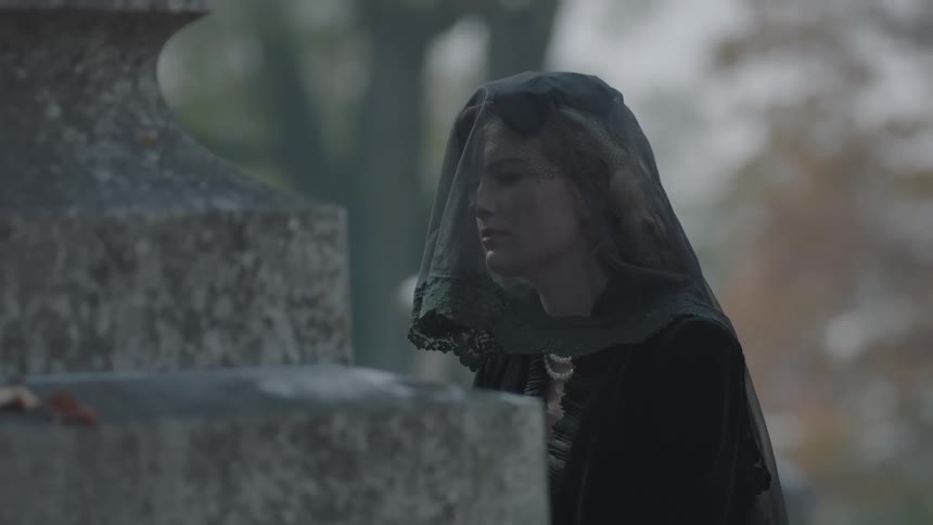 A woman holds a rose by a grave