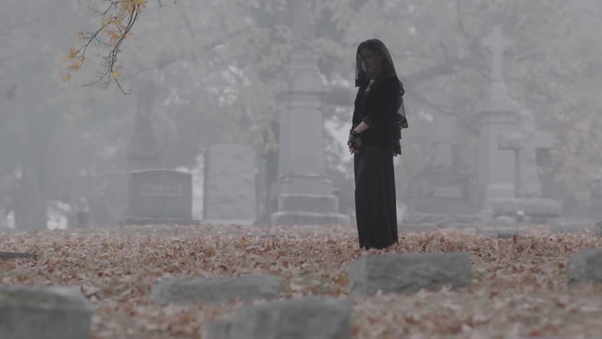 A veiled woman stands in a cemetery