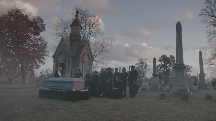 People are standing around a casket in a cemetery