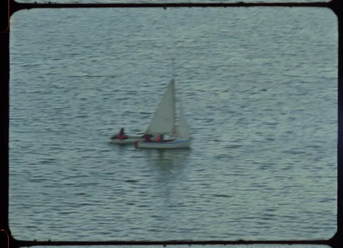 A sailboat pulls a smaller boat behind it in the ocean