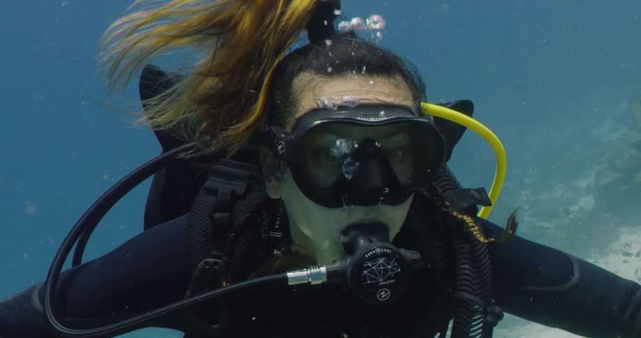 Female scuba diver releases many bubbles while floating near seafloor