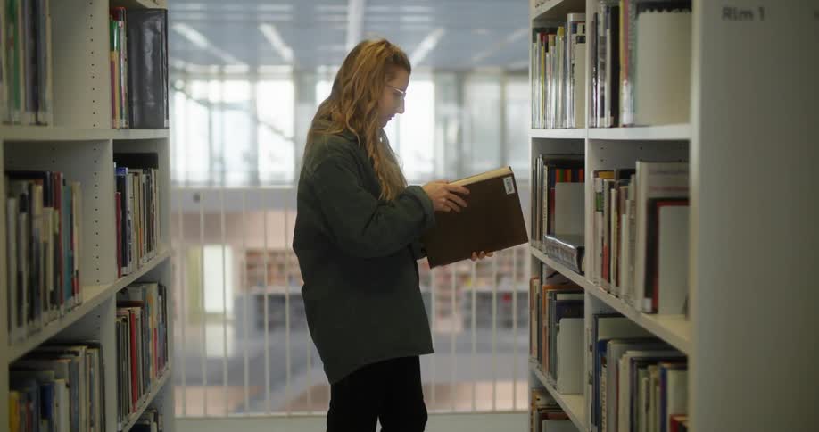 A young woman is looking at a book in a library