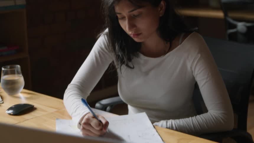 A woman sketches and takes notes while sitting in front of her computer