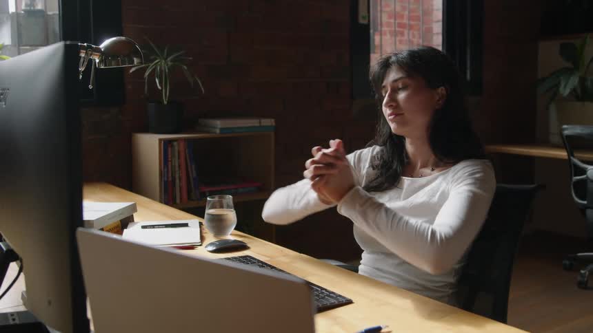 A woman stretches her arms out while typing on her computer