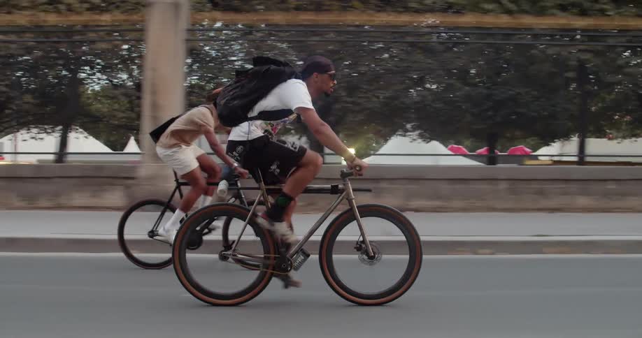 Two male cyclists pedal along road while a pedestrian walks in the opposite direction