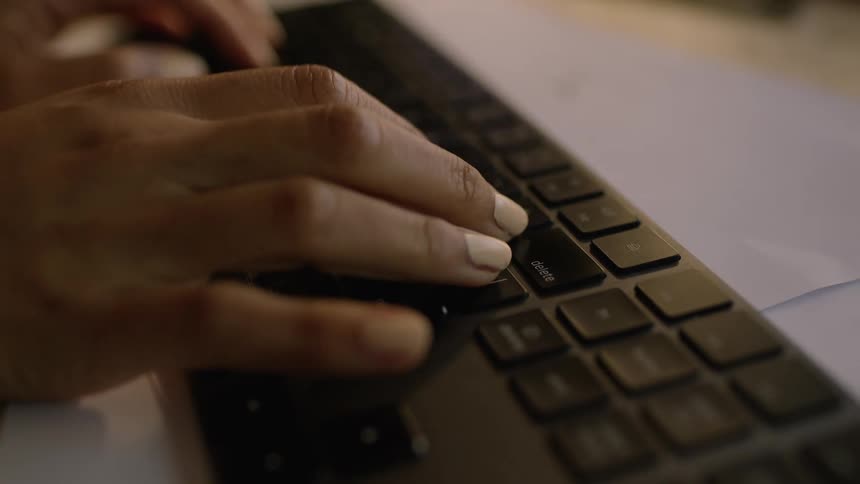 Womans hands typing on a black wireless keyboard on a white table
