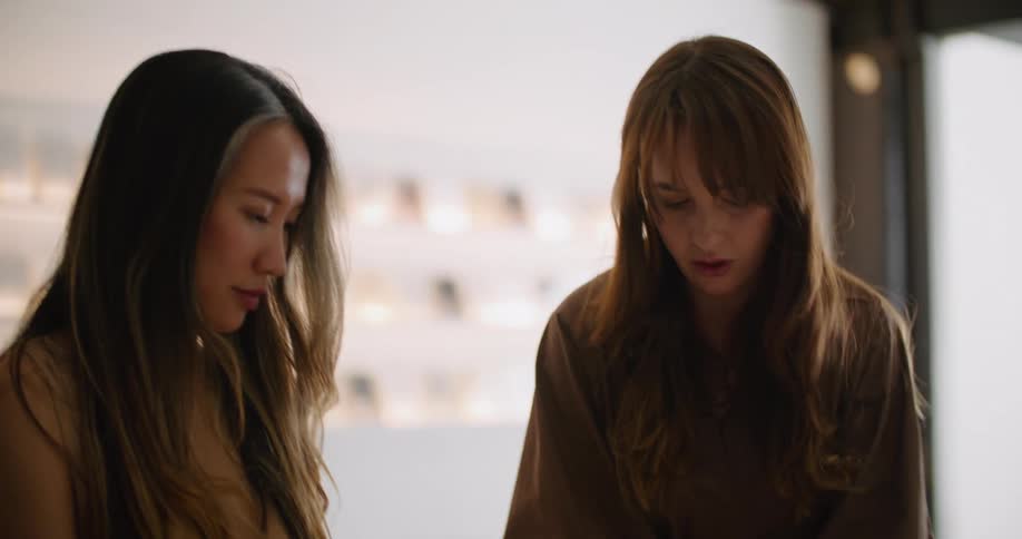Two women are standing in a store and one woman is pointing to a book in her hand as she talks to the other woman