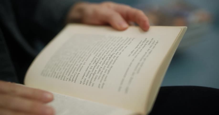 A man sits and reads a book on a bench