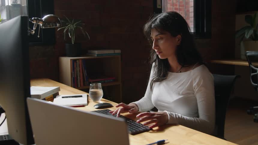 A woman is typing on her computer while sitting at home