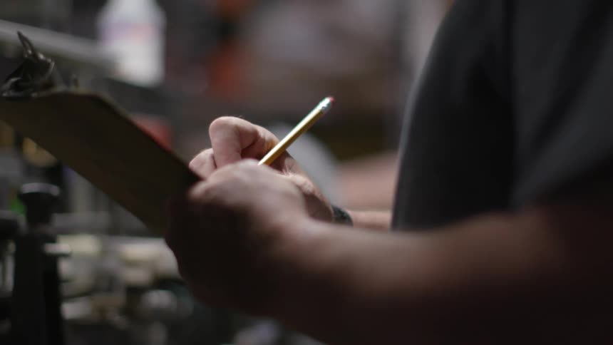 Two men stand in some kind of tool or hardware shop while one takes down notes on a clipboard