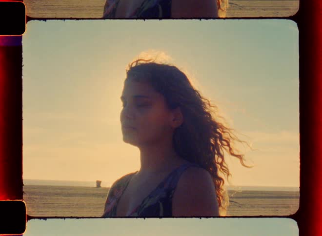 Young woman standing 100 yards from shore at the beach at sunset back lit with breeze blowing through her long wavy auburn hair