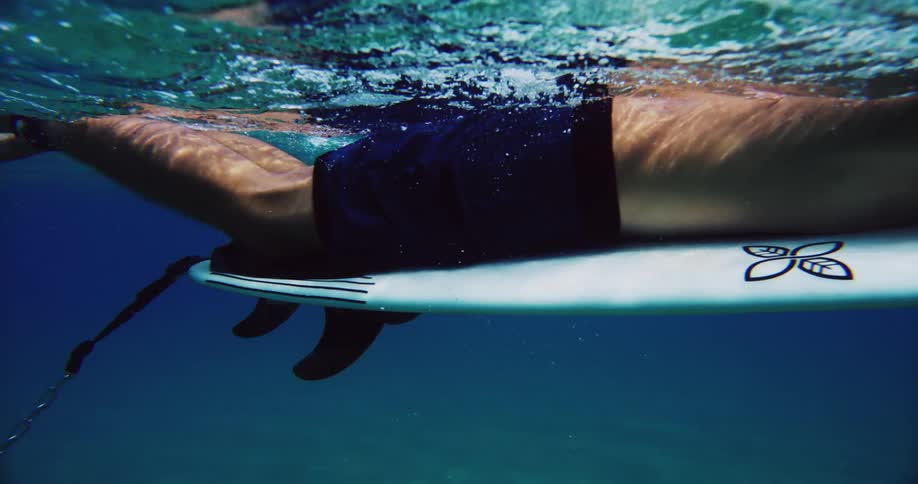 A surfer is paddling on his surfboard