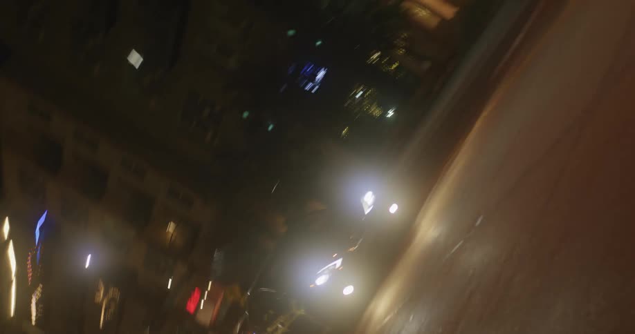 Traffic moves on a downtown street at night as lights glow in the darkness