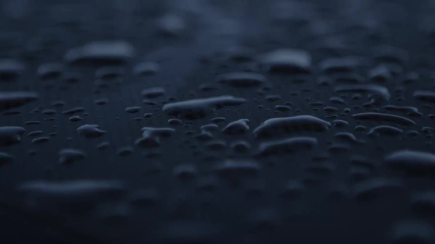 Close up of water droplets resting on the roof of a car parked outdoors at morning