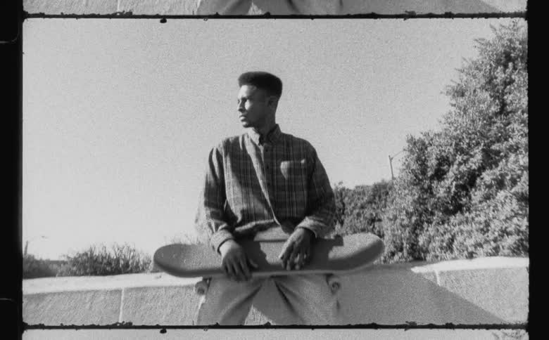 A man sits on a wall with his skateboard in his lap
