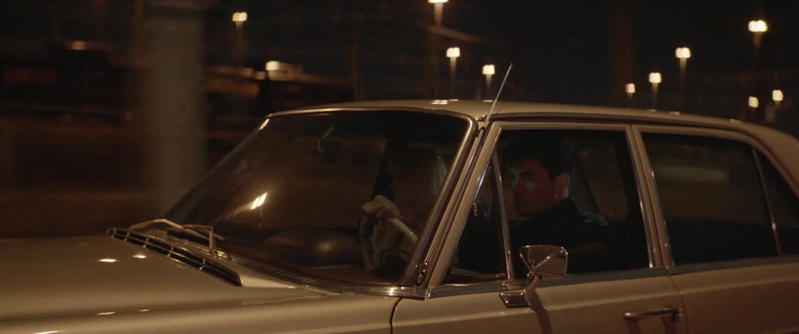 Young fashionable couple on a vintage car driving in the city street at night