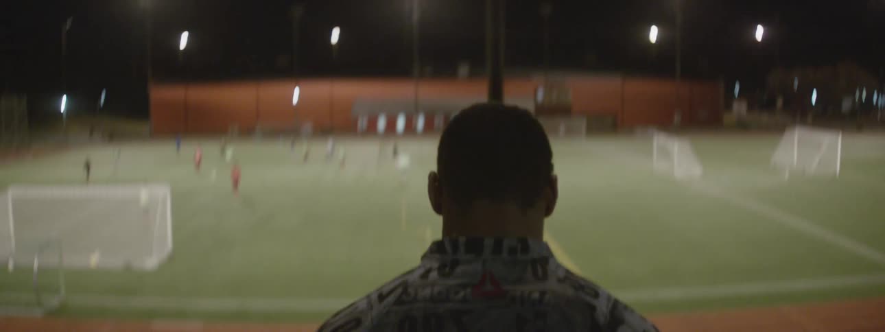 A man runs down the steps in a stadium where people are playing soccer