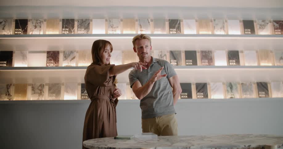 A man is standing in a store talking to the sales woman and pointing as they talk