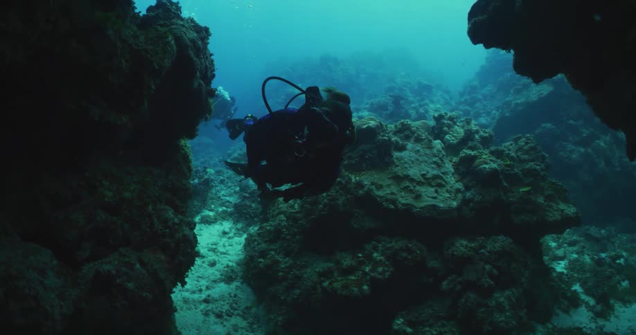 Scuba divers swimming through rocky coral underwater