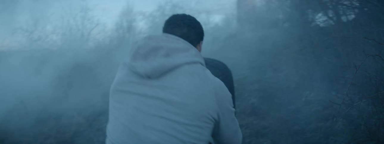 A man struggles to push a huge tire uphill in a smoggy wooded area