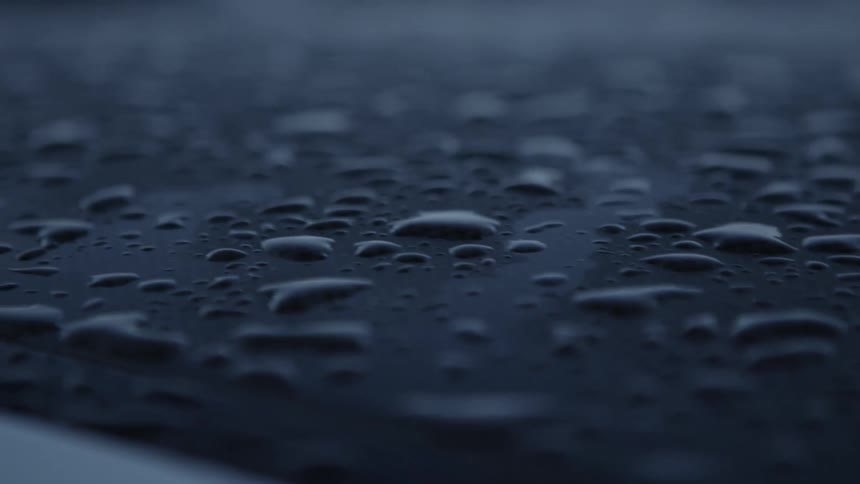 Close up of water droplets resting on the roof of a car parked outdoors at morning
