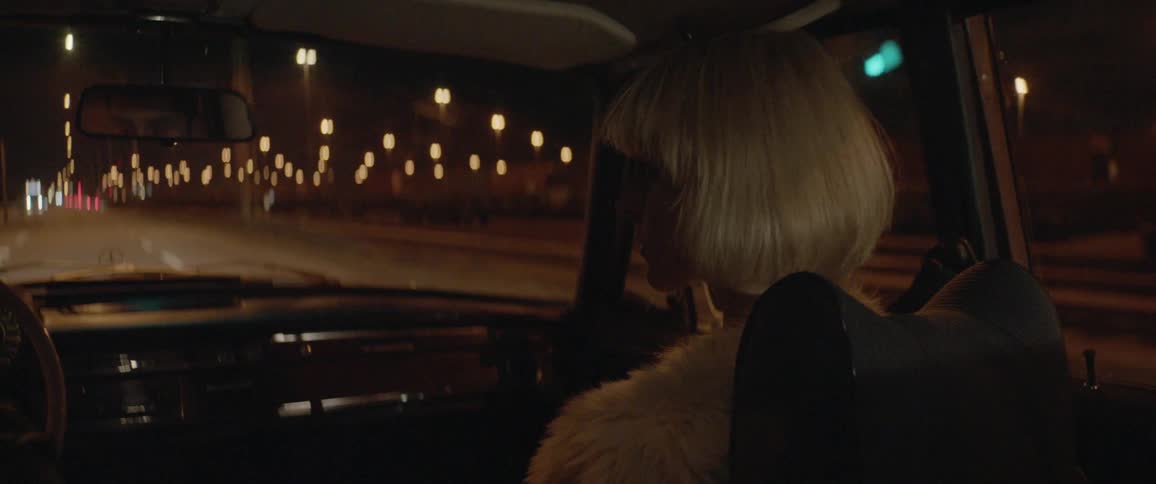 Blonde woman sitting in passenger seat of car at night watches driver
