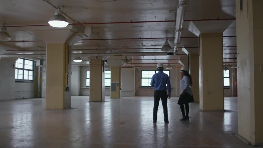 A man and woman walking through an empty building with hard hats on