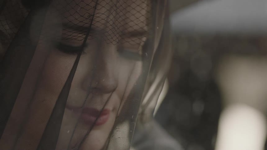Rain falls around a veiled and mourning woman