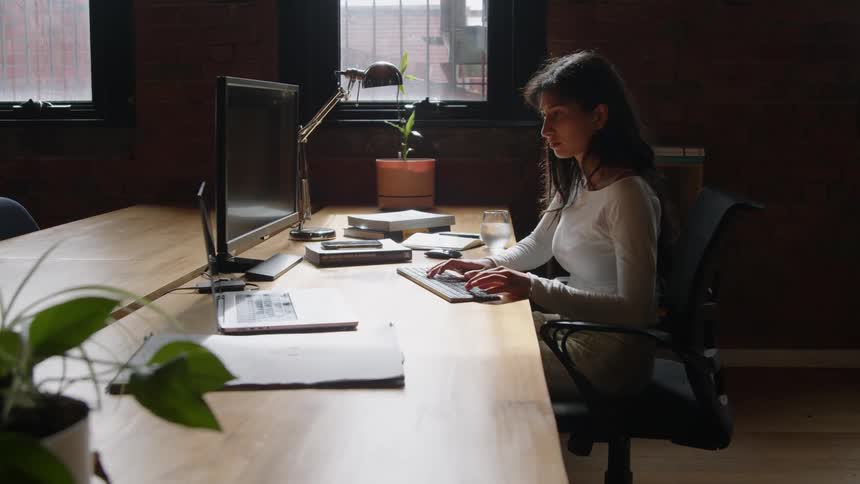 A woman is sitting at a desk and typing on computer