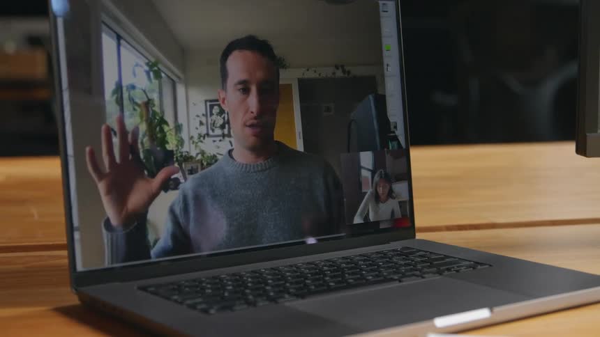 Woman makes video call with man in gray sweater on laptop taking notes in room
