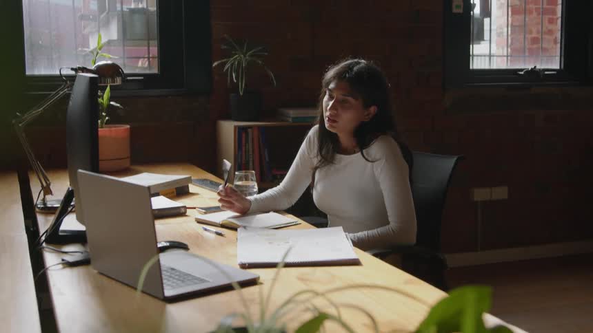 A woman is sitting at her computer desk and talking to someone