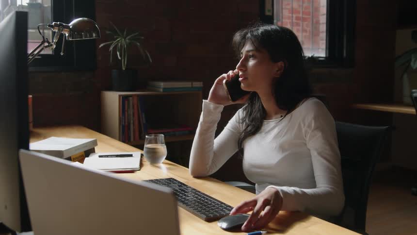 A young woman is working in the office and talking on the phone