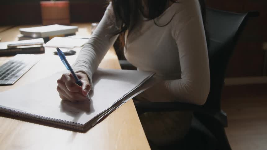 A woman writes on a large notepad while sitting at a desk in an office during the day