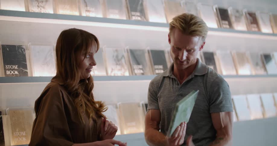 An employee is showing a customer a floor or wall sample inside of a store