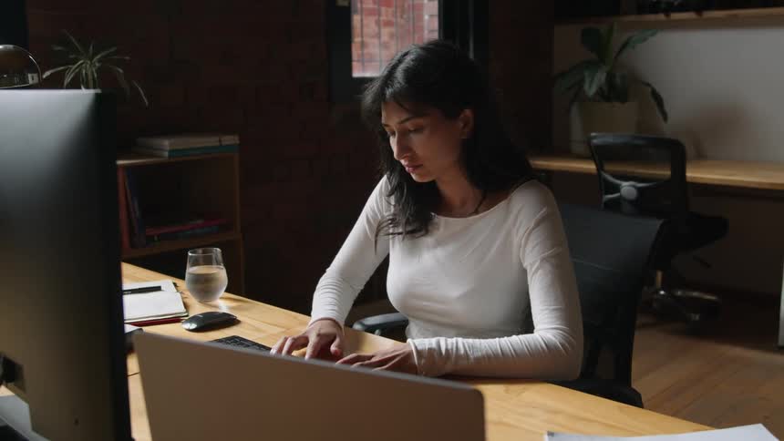 A woman sitting at a desk in front of her computers typing