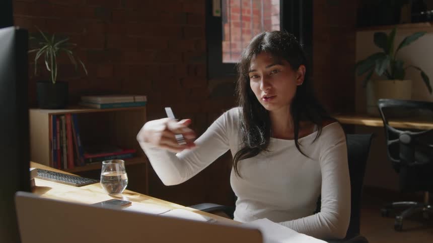 A woman takes notes and chats with someone on a video call using her laptop