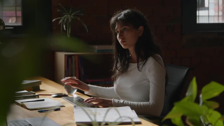 A woman types on a keyboard while sitting at a desk