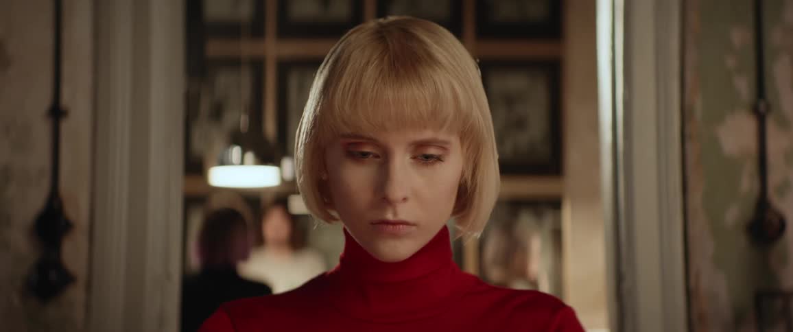 A woman is looking down with a stoic look on her face and then looks straight at the camera with the same expression